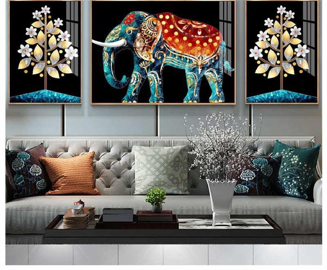 Three-piece set of a jewelled ceremonial elephant flanked by trees of gold and white blossom, above a grey tufted sofa
